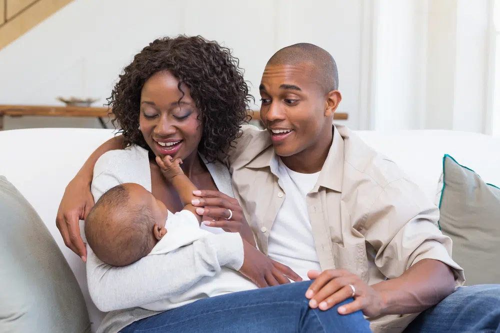 Happy young parents spending time with baby on the couch at home in the living room
