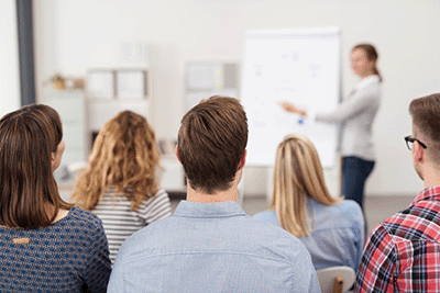 Rear View of Young Office Workers in Casual Outfits Listening to a Top Manager Explaining Something Using Illustrations_